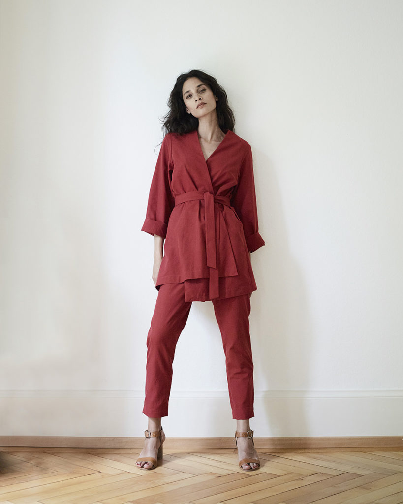 Karen trägt eine rote, asymmetrische Kimonojacke in rotem Baumwollstoff mit passender Hose. Sehr schlicht ohne Details.  Handgefärbter und handgewebter Baumwollstoff von kleinen Familienbetrieben in Indien.