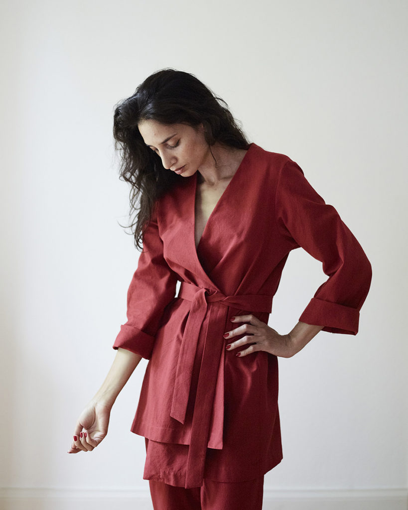 Karen trägt im Lookbook eine rote, asymmetrische Kimonojacke in rotem Baumwollstoff mit passender Hose. Sehr schlicht ohne Details.  Handgefärbter und handgewebter Baumwollstoff von kleinen Familienbetrieben in Indien.